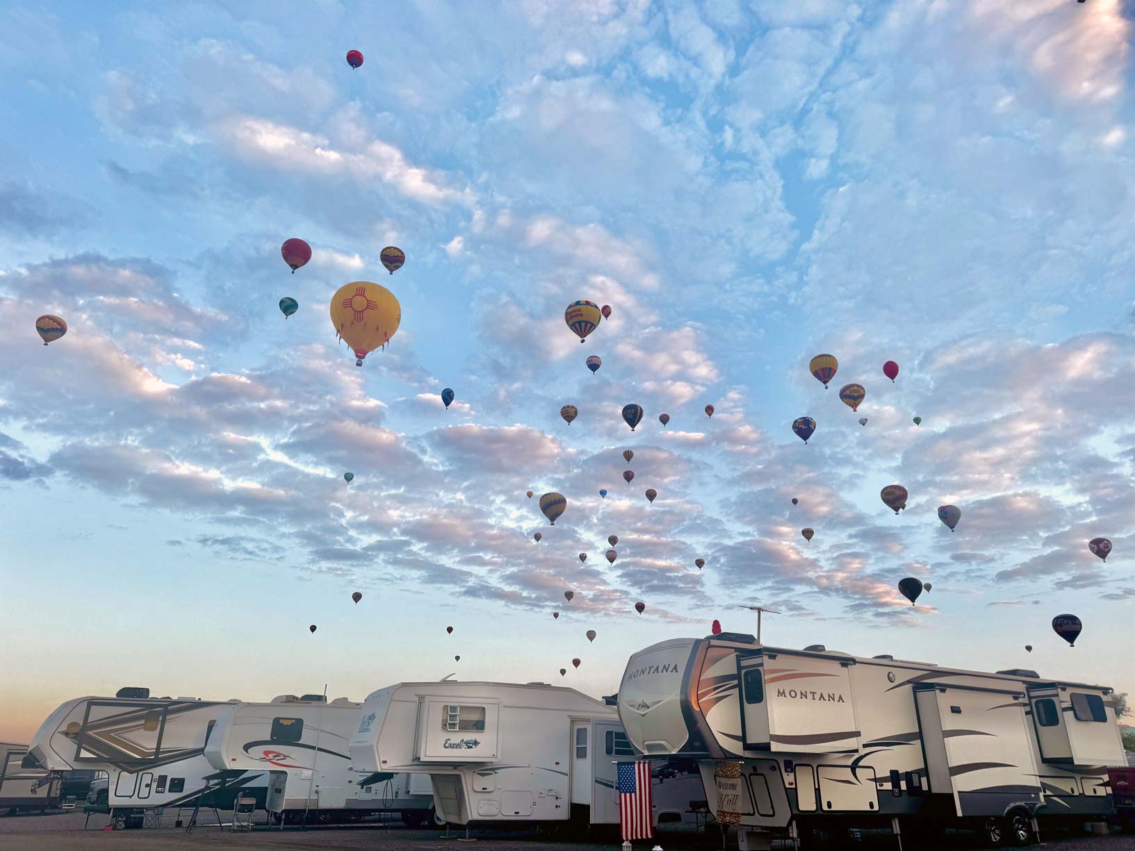 RVs parked at the Albuquerque International Balloon Fiesta with hot air balloons in the background.